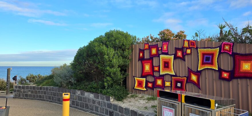Granny squares on a beach fence, the sea on the horizon